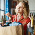 Mulher sorrindo segurando uma sacola de compras vintage de um brechó.